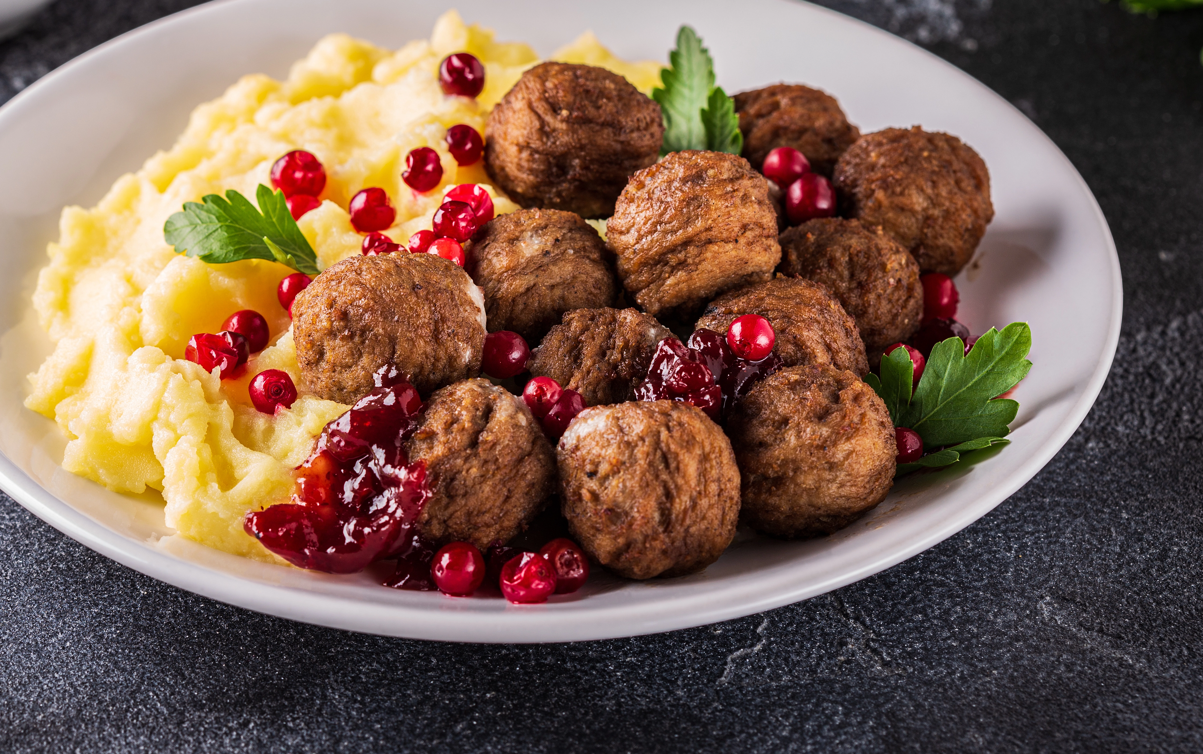 Köttbullar, lingon och mos på en vit tallrik i närbild